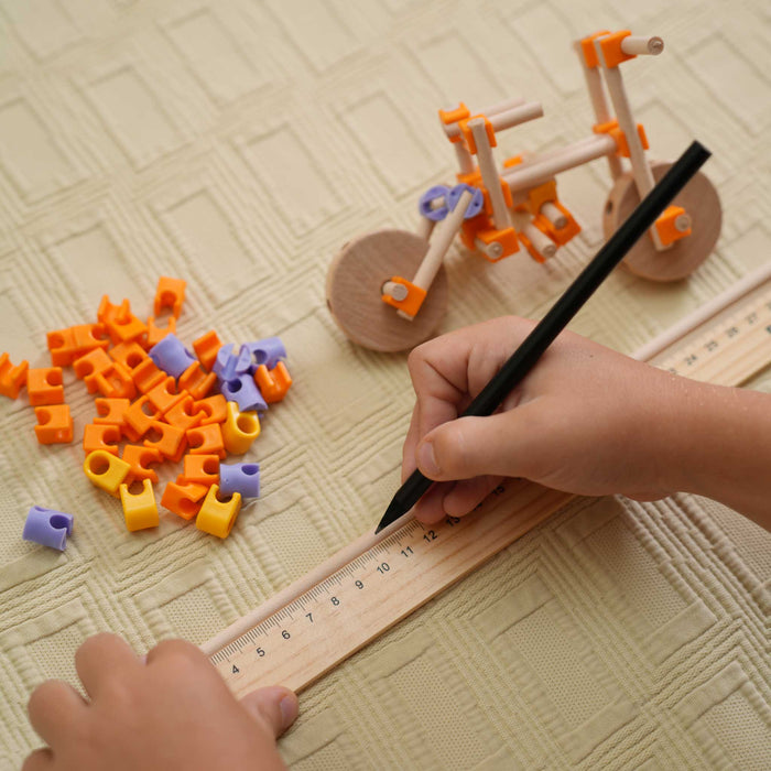 Child's hand using a ruler and pencil with building blocks on a textured from beaver