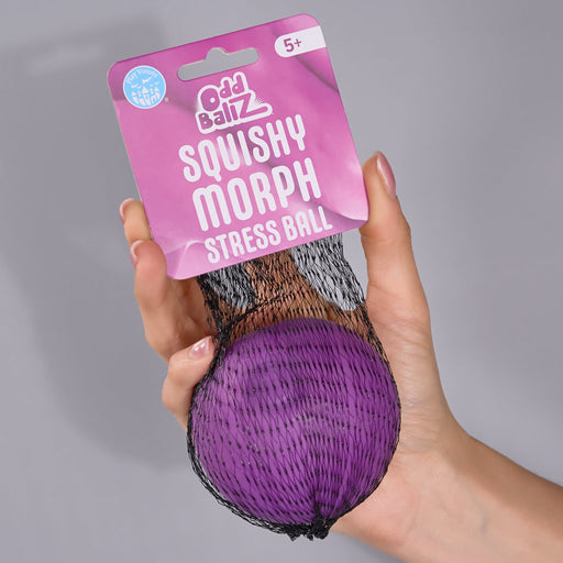 A hand holding an Odd Ballz Squishy Morph Stress Ball in a purple mesh bag with a pink retail hanger, against a plain gray background.
