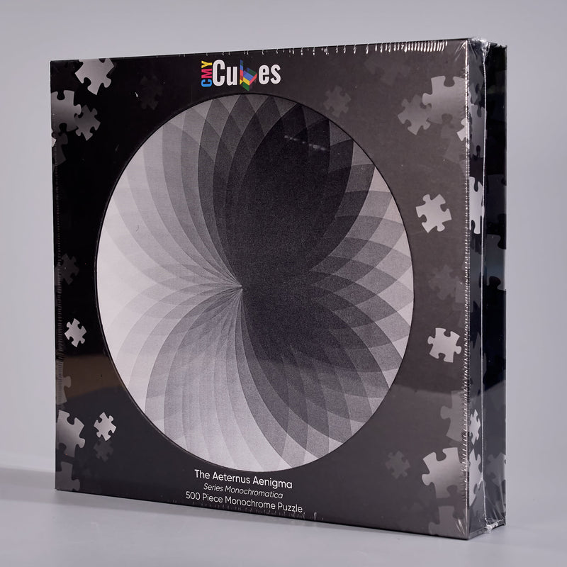 A boxed jigsaw puzzle package on a light gray studio background. The front shows a circular black-and-white optical illusion design with the brand name 'Cubes' at the top and text reading 'The Asterus Aenigma 500 Pieces Monochrome Puzzle'.