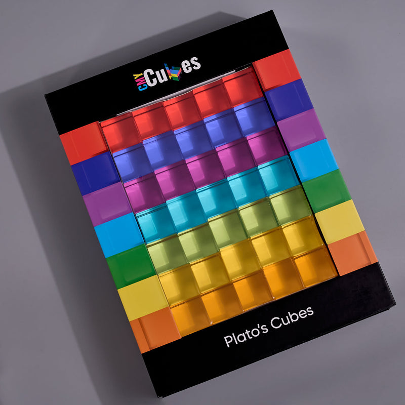A boxed set of plato's cubes translucent Platonic-style cubes arranged in a rainbow gradient on a black retail box, photographed at an angle on a gray background. The box shows the brand name 'eCubes' at the top and 'Plato's Cubes' at the bottom.