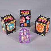 Three black retail boxes labeled 'Super Squeeze Glitter' and 'Capybara' arranged around a small glittery capybara figure in the foreground on a light gray studio background.