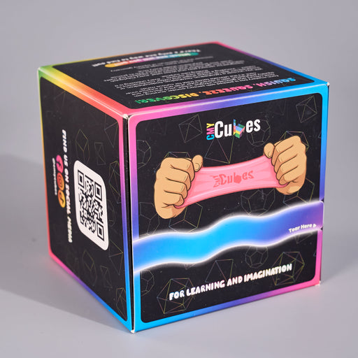 A cube-shaped product box for 'CMY Cubes' featuring a black front panel with an illustration of hands stretching a pink elastic band, surrounded by a vibrant iridescent rainbow border on a neutral gray background.