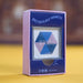 A boxed product labeled 'SPECTACULARLY MAGNETIC' standing upright on a yellow surface with a blurred brown background. The package is pink and dark blue, with a clear window showing a hexagonal magnetic bead arrangement in blue and pink.
