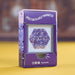 A purple product box labeled 'SPECTACULARLY MAGNETIC' with a clear window showing a hexagonal arrangement of small magnetic beads. The box has pixel-style side graphics and social media icons near the bottom, standing on a yellow surface against a blurred brown background.