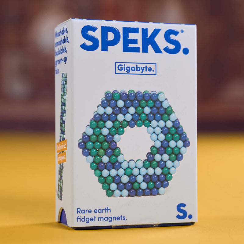 A box of SPEKS. Gigabyte Rare earth fidget magnets, model S, standing on a yellow surface with a blurred brown background.