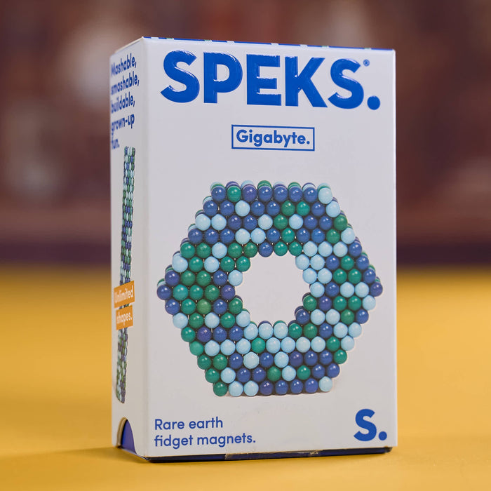 A box of SPEKS. Gigabyte Rare earth fidget magnets, model S, standing on a yellow surface with a blurred brown background.