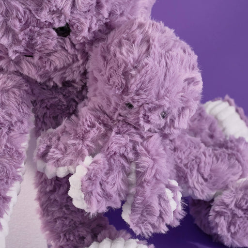 Purple adorable baby plush octopus, soft fluffy texture, lavender color, cute smiling face, long tentacles, white rope-detail accents, cuddly stuffed toy, raised display, close-up product focus.