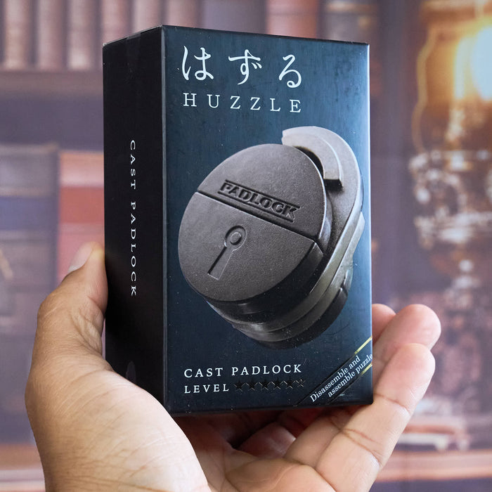 HUZZLE CAST PADLOCK Hand holding a Huzzle cast padlock packaging box with a blurred background