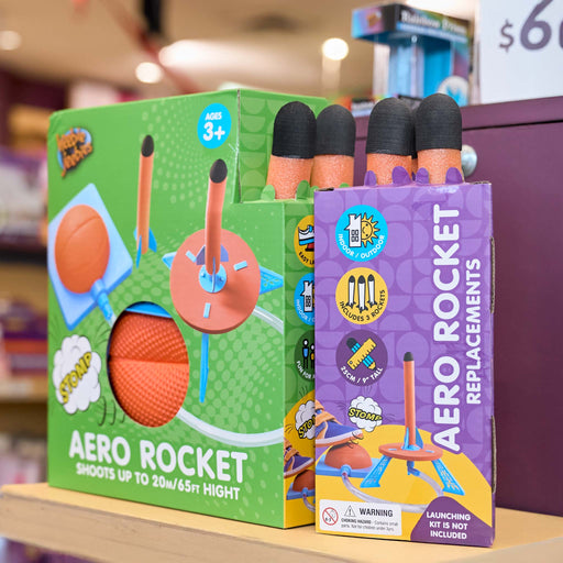 A retail display of Pop Rocket Aero Rocket toy set, showing the green original box, a purple box of foam rocket replacements, and several orange foam rockets with black tips on a store shelf.