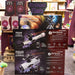 Three retail boxes of Celestron StarSense Explorer LT telescopes stacked on a store display, with a larger Saxon 15-70Z reflector telescope visible in the center box and additional toy boxes in the background.