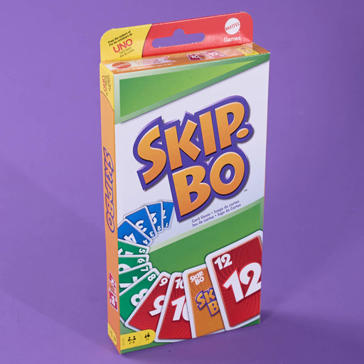 A boxed card game called Skip-Bo, photographed upright against a solid purple background. The box is mostly white with large orange and blue Skip-Bo lettering, plus green and yellow sections and sample card graphics showing red, green, blue, and orange cards.