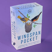 The product is a boxed card game called Wingspan Pocket, shown standing upright on a solid purple background. The box features an illustration of birds and a nest on a light blue sky background, with the title 'WINGSSPAN POCKET' in large blue letters.
