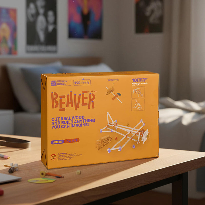 A yellow-orange product box labeled 'BEAVER' sits on a wooden table in a softly blurred bedroom or playroom setting. The box shows a wooden airplane model and text including 'CUT REAL WOOD AND BUILD ANYTHING YOU CAN IMAGINE!' and '10 CRAFTERS, 1000+ PIECES.