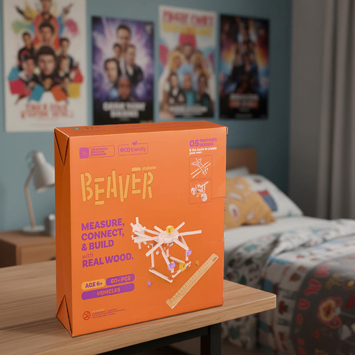 An orange cardboard product box for a toy set labeled 'BEAVER' sits on a wooden table in a bedroom. The box features purple and yellow text and a small white wooden vehicle illustration.