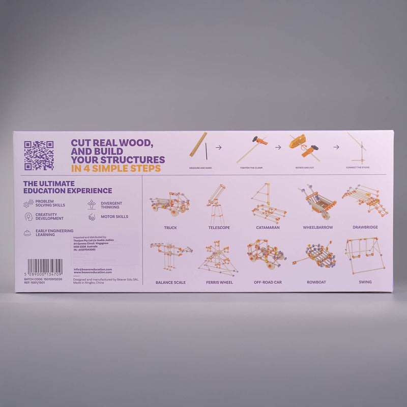 The product packaging box for an educational wood model kit, displayed against a neutral gray background. The box is light pink with purple and orange text and diagrams showing how to build structures like a track, telescope, and car.