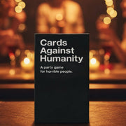 Cards Against Humanity game box on a table with blurred people and lights in the background