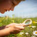 Child examining flowers through a magnifying glass in a field