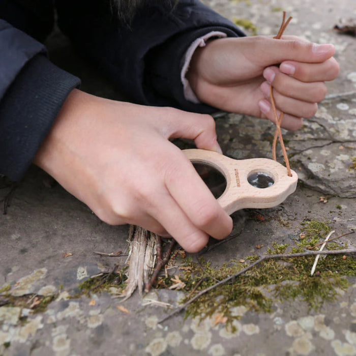 Child examining a flower through a magnifying glass in a field