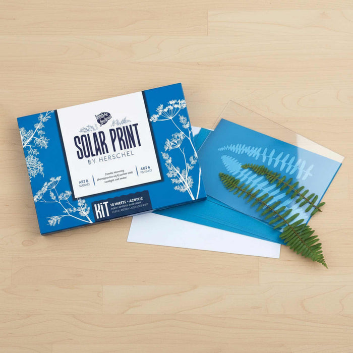 Solar print kit with blue packaging and a sheet of solar prints on a wooden surface