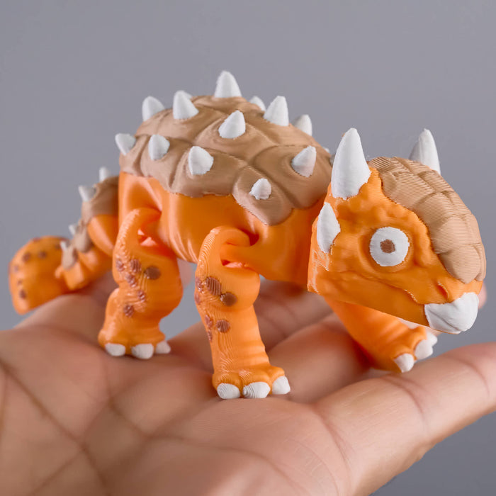 Small orange dinosaur figurine with spikes held in a hand against a gray background