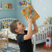 Child holding a DIY clock in a colorful bedroom with toys and furniture.