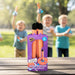A purple retail box of Rocket Verbe Aerodynamic Rocket Replacements stands on a wooden table outdoors, with three blurred children holding orange rockets in a park behind it.