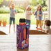A boxed toy product labeled 'AERO ROCKET REPLACEMENTS' stands on a wooden table in a real outdoor porch/garden setting, with children blurred in the background playing. Because a real environment and people are present, this is Lifestyle rather than Product/Packaging, even though the product box is prominently shown.
