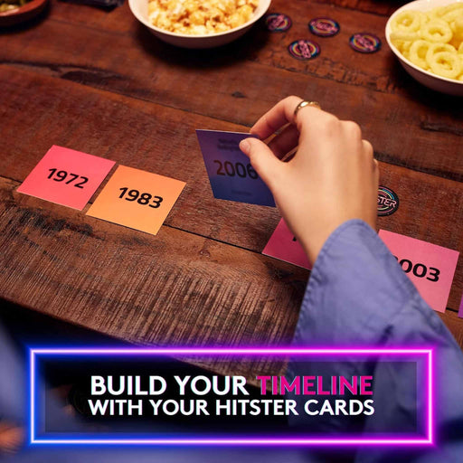 Hand placing a card on a wooden table with other cards displaying years, surrounded by snacks.