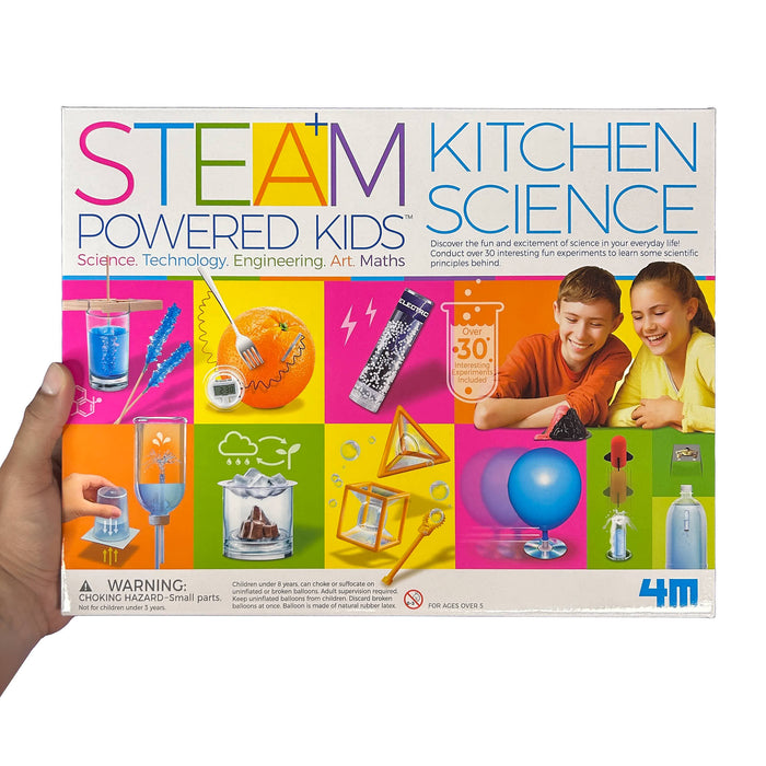 Box of 'STEAM Powered Kids Kitchen Science' kit held by a hand on a white background