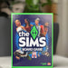 The Sims board game box with characters and logo on a blurred background