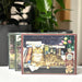 Cobble Hill puzzle box with a cat and books illustration on a surface with plants in the background