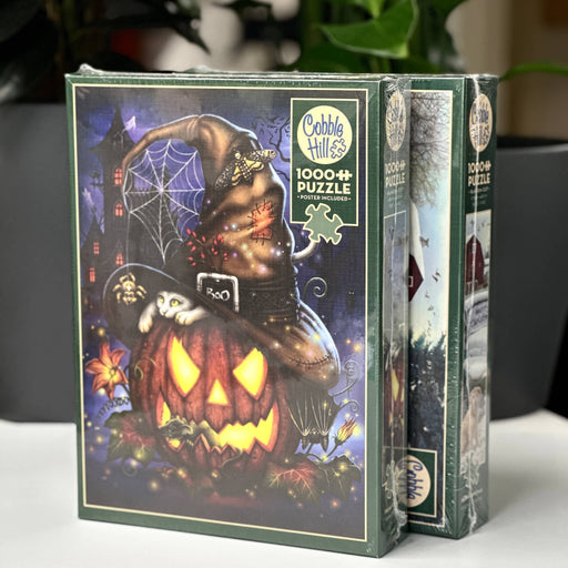Two Halloween-themed puzzle boxes by Cobble Hill on a white surface with a blurred background.