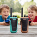Two kids smiling in the background while two toy walkie-talkies stand on a wooden table in the foreground. The walkie-talkies are branded KIDYWOLF, with one in teal and one in tan.