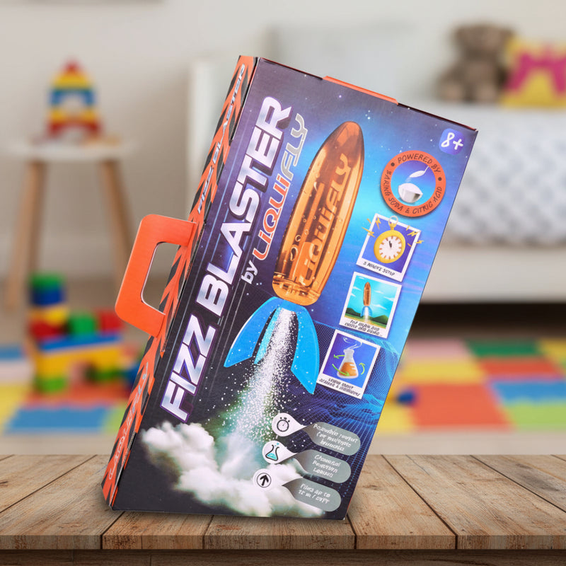 Fizz Blaster by Liquifly toy packaging on a wooden table with colorful toys in the background