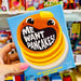 Card game box titled 'Me Want Pancakes!' held in a hand with a colorful store background.