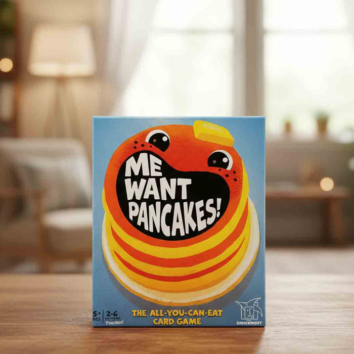 Card game box titled 'Me Want Pancakes!' on a wooden table with a blurred indoor background