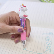 Hand holding a pink cartoon unicorn pen over a notebook