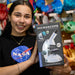 Person holding a microscope packaging with a NASA shirt in the background