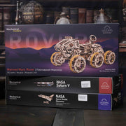NASA-themed mechanical models packaging on a wooden surface Boxed mechanical model of a Mars rover with UGears branding on a dark background.