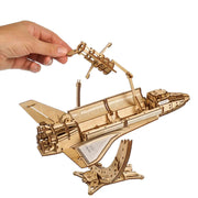 NASA-themed mechanical models packaging on a wooden surface Wooden model airplane kit with a hand holding a part against a white background