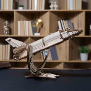 NASA-themed mechanical models packaging on a wooden surface Wooden model of a space shuttle on a stand with a bookshelf in the background
