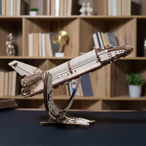 NASA-themed mechanical models packaging on a wooden surface Wooden model of a space shuttle on a stand with a bookshelf in the background