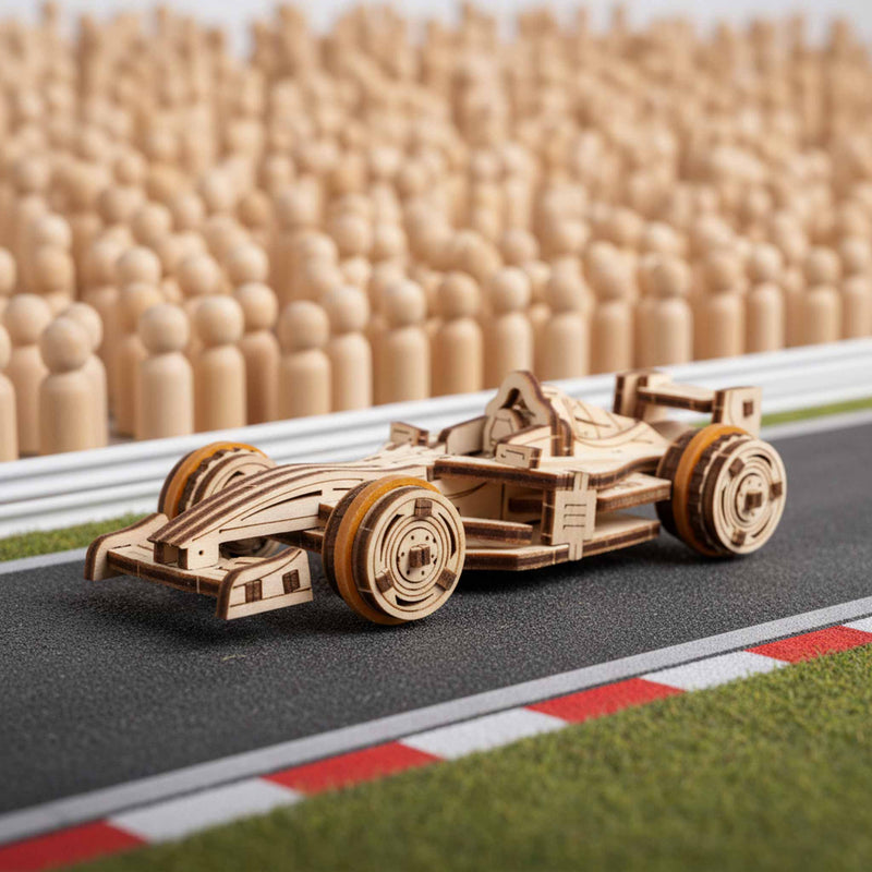 Ugears Compact Racer model Wooden model of a race car on a miniature racetrack with wooden stands in the background.