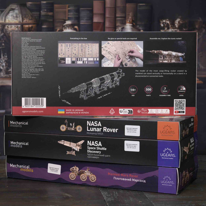 Stack of UGears NASA mechanical model boxes on a dark surface with a blurred background.