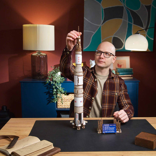 Model of a NASA Saturn V rocket with Man holding a model of a rocket on a desk 