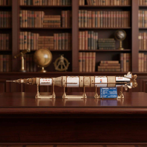 Ugears NASA Saturn V rocket Model rocket on a stand with a NASA label in front of a bookshelf