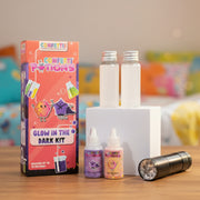 Glow in the dark kit with packaging, bottles, and flashlight on a pink background