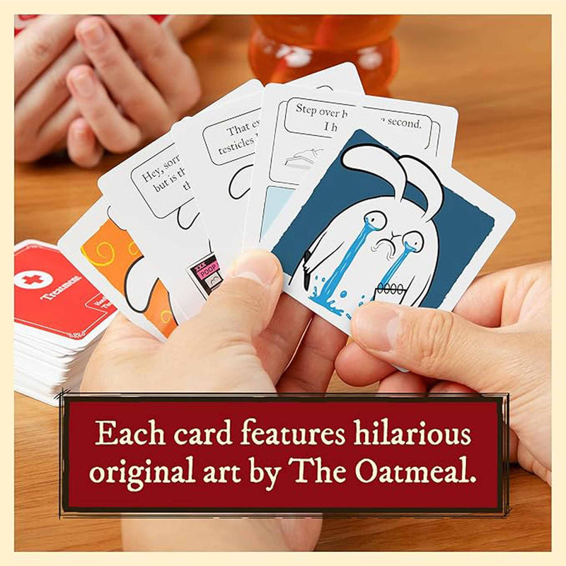 Hand holding a card with humorous art by The Oatmeal on a wooden surface.