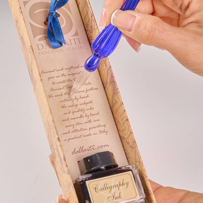 Calligraphy ink bottle with blue cap held by a hand, displayed in a decorative box.