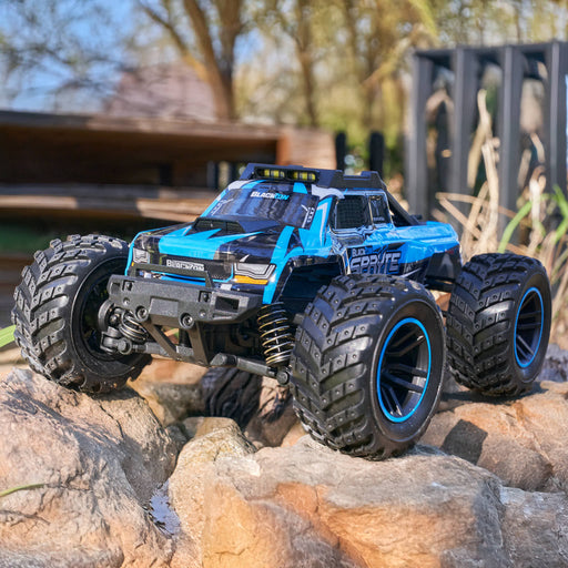 Blue and black remote control monster truck on rocky terrain with trees in the background